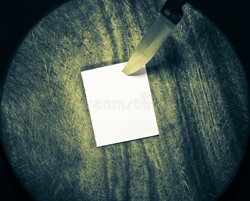 A piece of paper pinned by kitchen knife on circle wooden background. A piece of paper pinned by kitchen knife on circle wooden background.