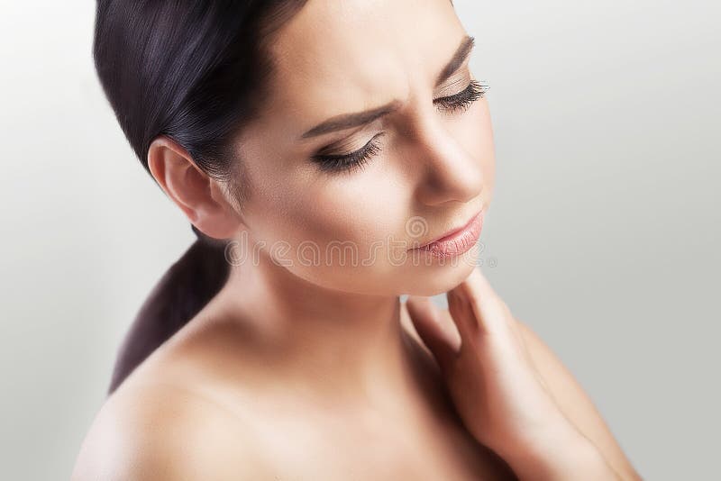 Neck pain. Tension after the working day. Sports injury to the neck. A young woman holds her hand to the neck. The concept of health. On a gray background