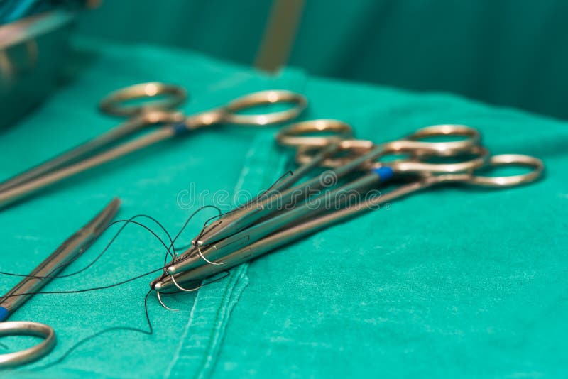 Needle Holders with Needles and Sutures and Scissors on Operating Table