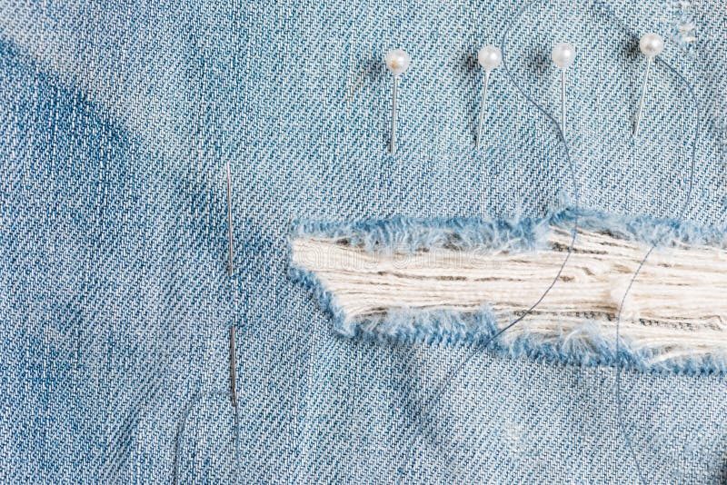 A needle and thread sew up a hole in a denim. Work of a seamstress or  tailor with a needle Stock Photo - Alamy