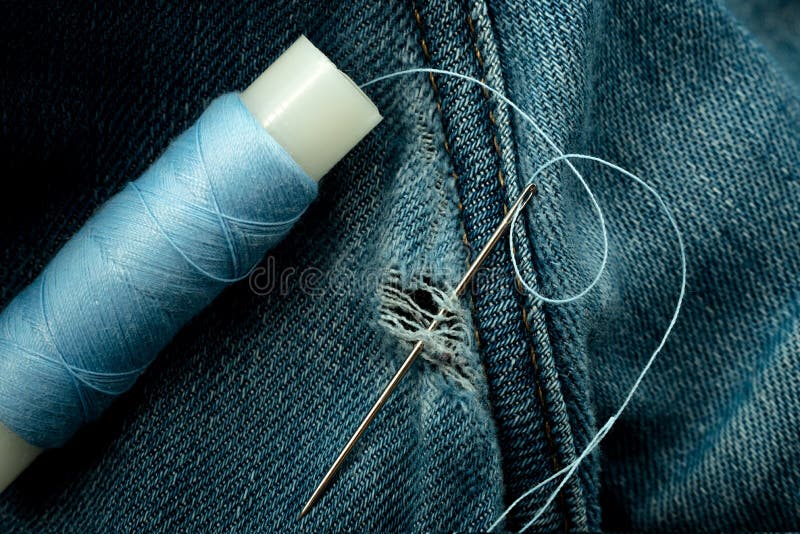 A Needle and Thread Sew Up a Hole in a Denim. Work of a Seamstress or