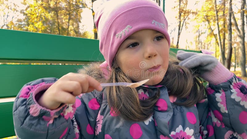 Neglected little hungry girl 4 years old in a pink hat and warm jacket eating marshmallows outdoor