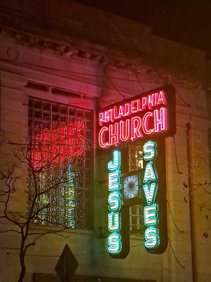 Neon Sign on Clark Street in Andersonville at night. The neon lights are reflected in the large glass window of the church. There&#x27;s a tree with bare branches. Neon Sign on Clark Street in Andersonville at night. The neon lights are reflected in the large glass window of the church. There&#x27;s a tree with bare branches.