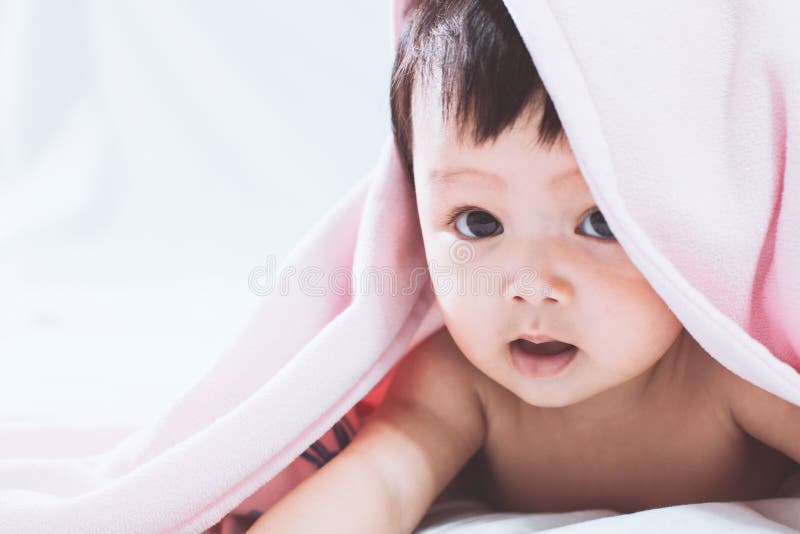 Neonata asiatica sveglia che sorride sotto la coperta rosa fotografia stock libera da diritti Neonata asiatica sveglia che sorride sotto la coperta rosa fotografia stock libera da diritti