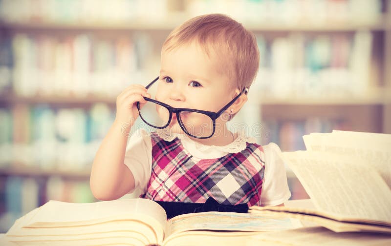 Neonata divertente in vetri che legge un libro in una biblioteca fotografia stock libera da diritti