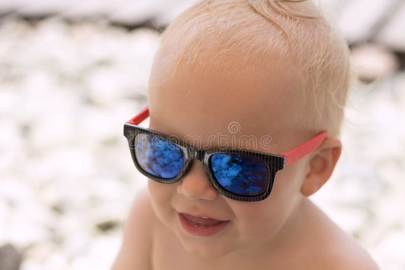 Neonato sorridente divertente in occhiali da sole sulla spiaggia Le pietre sono riflesse nei vetri Piccolo capo sulla vacanza fotografie stock Neonato sorridente divertente in occhiali da sole sulla spiaggia Le pietre sono riflesse nei vetri Piccolo capo sulla vacanza fotografie stock