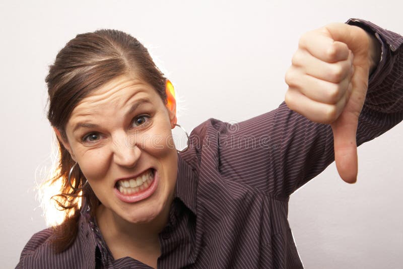 Young woman shows an agressive thumb down sign while fletching her teeth. Young woman shows an agressive thumb down sign while fletching her teeth.