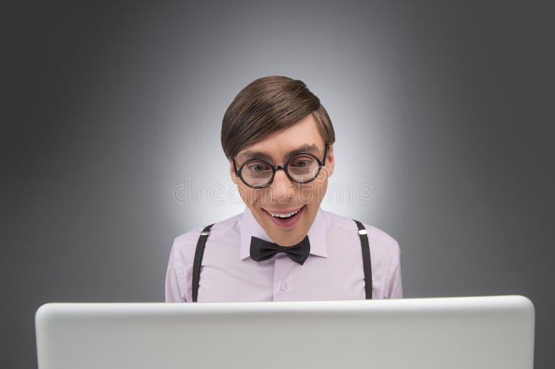Nerd at the computer. Young nerd man working at the computer while isolated on grey stock image Nerd at the computer. Young nerd man working at the computer while isolated on grey stock image