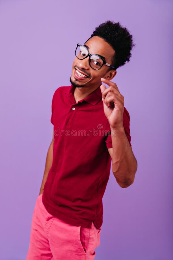 Nero entusiasta che si pone con un sorriso felice. studio di un giovane africano ispirato in occhiali alla moda.