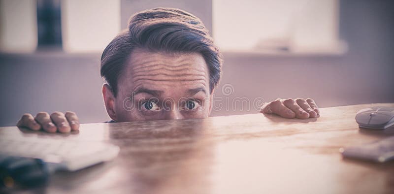 Nervous businessman peeking over desk royalty free stock photography Nervous businessman peeking over desk royalty free stock photography