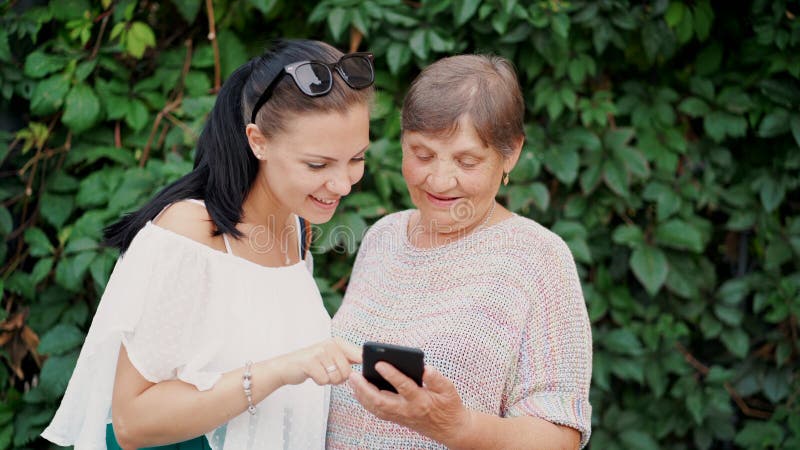 A neta mostra a avó idosa algo no smartphone, ensina-a segurar com dispositivo moderno e tecnologia imagens de stock royalty free A neta mostra a avó idosa algo no smartphone, ensina-a segurar com dispositivo moderno e tecnologia imagens de stock royalty free