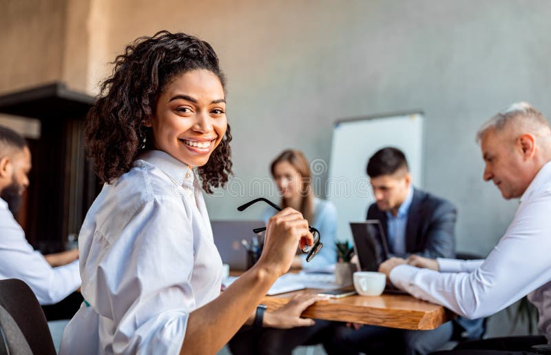 Nette afrikanische Geschäftsfrau, die mit Geschäftspartnern sitzt im Büro lizenzfreie stockfotos