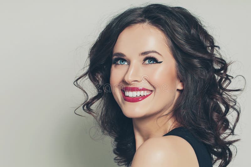 Nette brunette Frau mit gelockter Frisur lächelnd auf weißem Hintergrund lizenzfreies stockfoto
