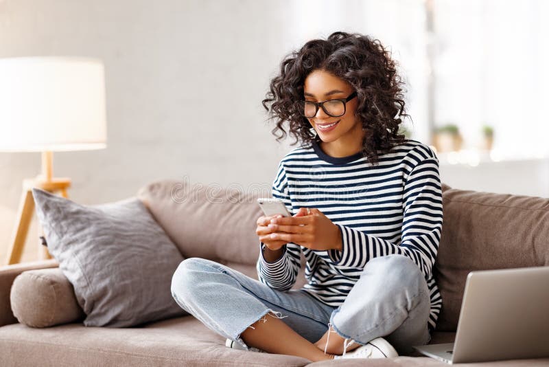 Nette ethnische Frau mithilfe des Smartphone auf Couch lizenzfreies stockbild