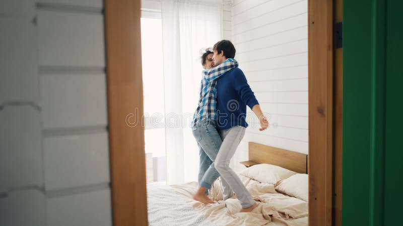 Nette junge Liebhaber tanzen auf das Bett zu Hause, das Spaß im Schlafzimmer hat und unvorsichtig lacht Glückliche Jugend, modern