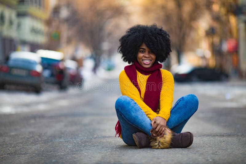 Fröhliche junge schwarze Frau sitzt mitten auf der Straße