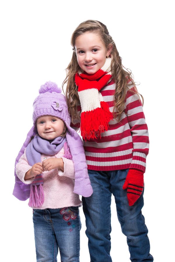 Nette lächelnde Schwestern, welche die bunte gestrickte Strickjacke, Schal, Hut und die Handschuhe lokalisiert auf weißem Hinterg lizenzfreie stockbilder
