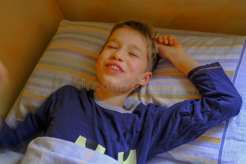 Netter blonder Junge in lächelndem in der Nahaufnahme des Betts morgens aufwachen Blue Pyjama. Kinderschlafzimmer. entspannen Sie stockfotos