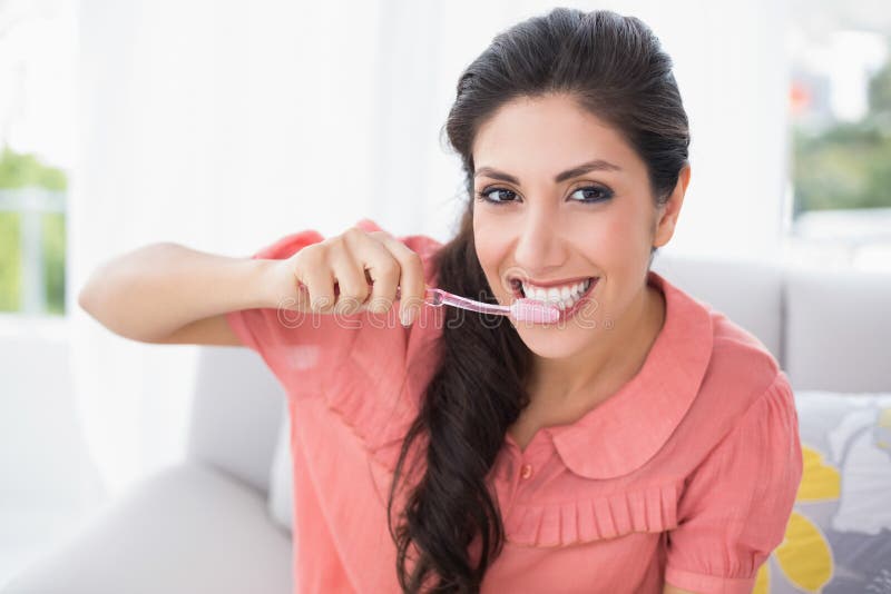 Netter Brunette, der auf ihrem Sofa putzt ihre Zähne sitzt stockfotos