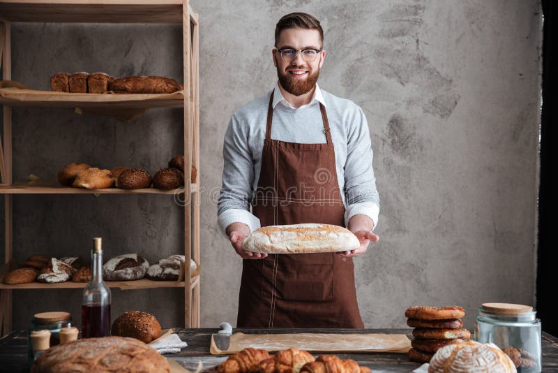 Netter Bäcker des jungen Mannes, der an der Bäckerei hält Brot steht