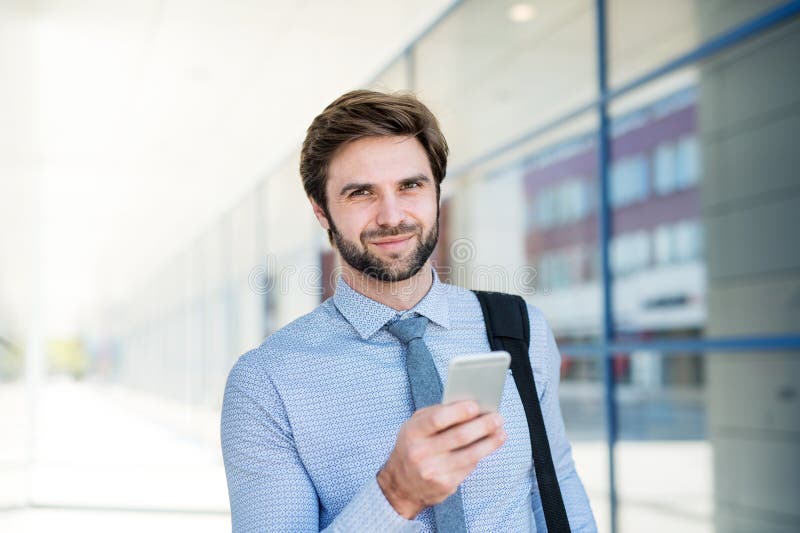 Handsome businessman scrolling on smartphone while walking on city street, going to office. Manager smiling, outdoor in urban setting. Handsome businessman scrolling on smartphone while walking on city street, going to office. Manager smiling, outdoor in urban setting.