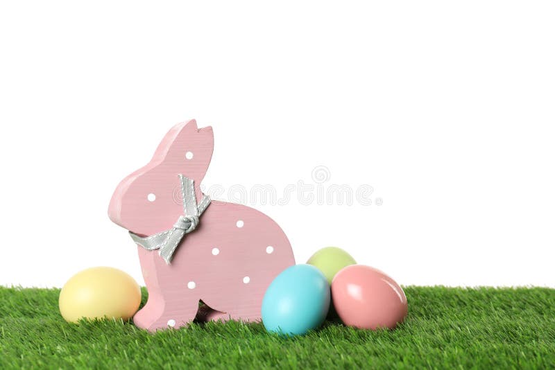 Netter hölzerner Osterhase und gefärbte Eier auf grünem Gras gegen weißen Hintergrund stockfotografie
