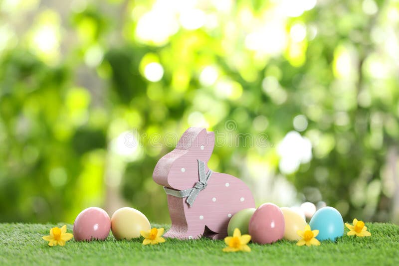 Netter hölzerner Osterhase und gefärbte Eier auf grünem Gras stockfoto