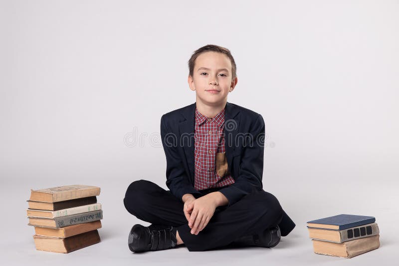 Netter Junge in einem Klagensitzen und -lesung ein Buch auf einem weißen Hintergrund stockbilder