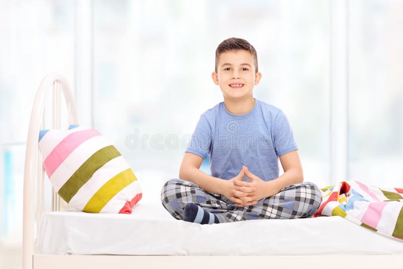 Netter kleiner Junge in den Pyjamas, die auf einem Bett sitzen lizenzfreies stockbild Netter kleiner Junge in den Pyjamas, die auf einem Bett sitzen lizenzfreies stockbild