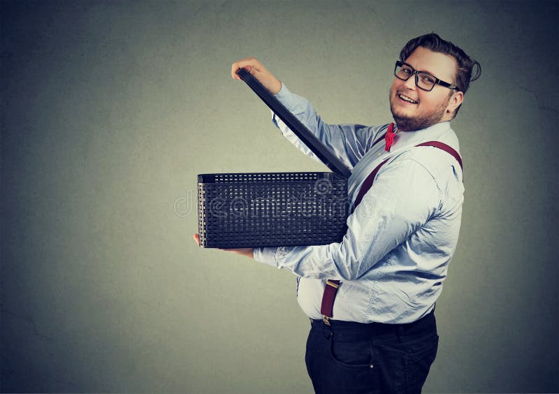 Side view of happy chubby man in glasses opening box releasing gifts and smiling at camera on gray. Side view of happy chubby man in glasses opening box releasing gifts and smiling at camera on gray