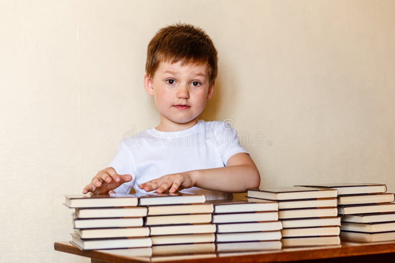 Netter sechsjähriger Junge, der an einem Schreibtisch mit Stapeln Büchern sitzt lizenzfreie stockbilder Netter sechsjähriger Junge, der an einem Schreibtisch mit Stapeln Büchern sitzt lizenzfreie stockbilder