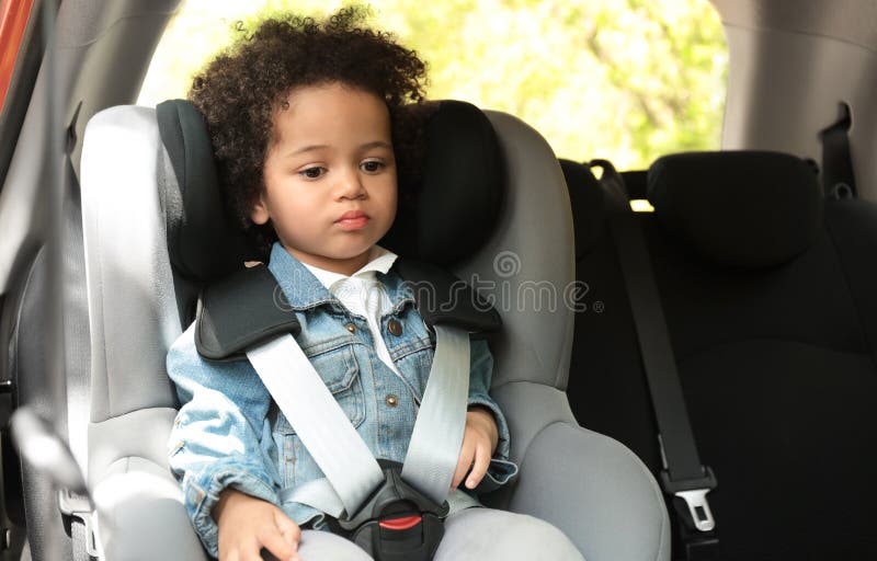 Nettes afro-amerikanisches Mädchen, das im Sicherheitssitz allein innerhalb des Autos sitzt lizenzfreie stockfotos Nettes afro-amerikanisches Mädchen, das im Sicherheitssitz allein innerhalb des Autos sitzt lizenzfreie stockfotos