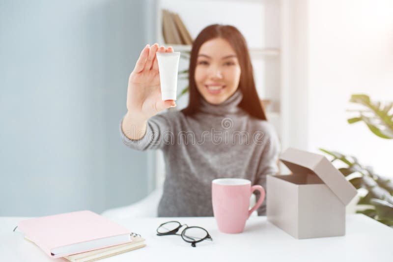 Nettes Bild des attraktiven Mädchens sitzend am Tisch und das Schönheitsprodukt zur Kamera zeigend Es ist Handcreme stockbilder Nettes Bild des attraktiven Mädchens sitzend am Tisch und das Schönheitsprodukt zur Kamera zeigend Es ist Handcreme stockbilder