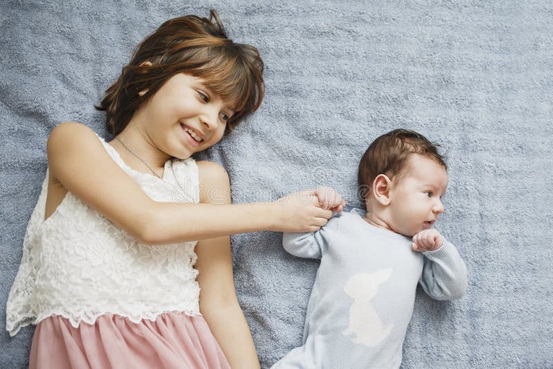 Nettes glückliches Mädchen, das ihren neugeborenen Babybruder hält Grauer Hintergrund Hübsches Baby in der blauen Kleidung lizenzfreies stockbild Nettes glückliches Mädchen, das ihren neugeborenen Babybruder hält Grauer Hintergrund Hübsches Baby in der blauen Kleidung lizenzfreies stockbild