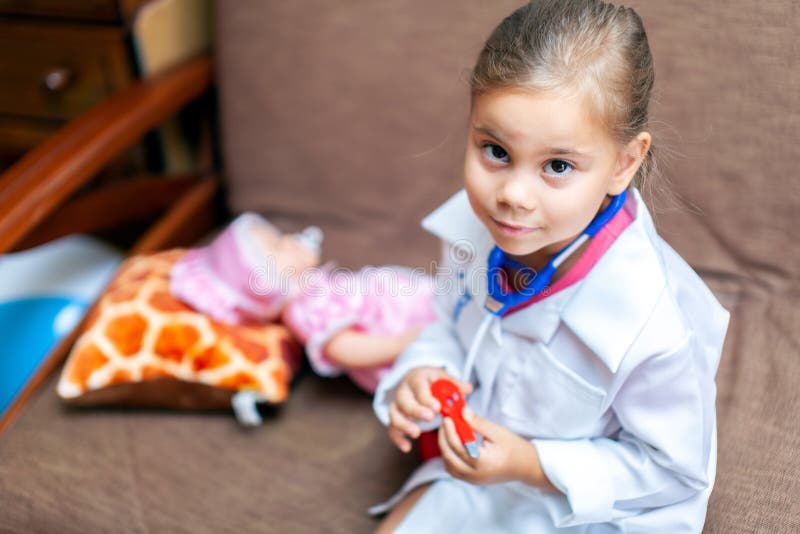 Nettes Kindermädchen, das Doktor mit Baby - Puppenspielzeug spielt lizenzfreie stockfotografie Nettes Kindermädchen, das Doktor mit Baby - Puppenspielzeug spielt lizenzfreie stockfotografie