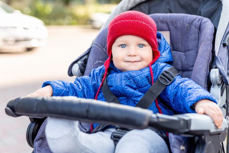 Nettes kleines Baby, das im Spaziergänger sitzt und während des Wegs am kalten Herbst- oder Wintertag lächelt Entzückendes Kinder lizenzfreie stockfotografie Nettes kleines Baby, das im Spaziergänger sitzt und während des Wegs am kalten Herbst- oder Wintertag lächelt Entzückendes Kinder lizenzfreie stockfotografie