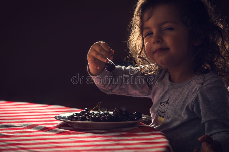 Nettes kleines Mädchen, das Kirschen zum sein Morgenfrühstück isst lizenzfreie stockfotografie Nettes kleines Mädchen, das Kirschen zum sein Morgenfrühstück isst lizenzfreie stockfotografie
