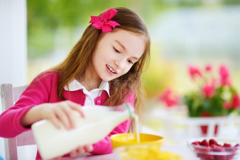 Nettes kleines Mädchen, das zu Hause ihr Frühstück genießt Hübsches Kind, das Corn Flakes und Himbeeren- und Trinkmilch vor Schul stockbild Nettes kleines Mädchen, das zu Hause ihr Frühstück genießt Hübsches Kind, das Corn Flakes und Himbeeren- und Trinkmilch vor Schul stockbild