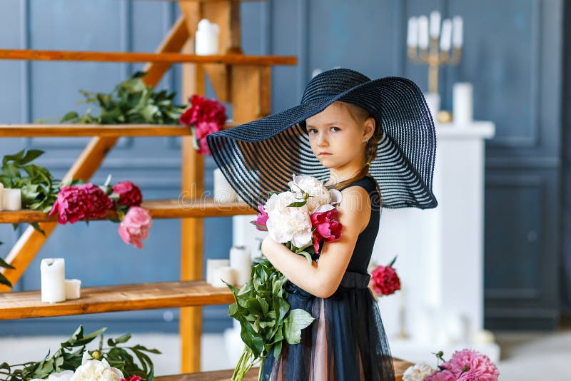 Nettes kleines Mädchen im Großen schwarzen Hut mit Pfingstrosen im Studio lizenzfreie stockfotos Nettes kleines Mädchen im Großen schwarzen Hut mit Pfingstrosen im Studio lizenzfreie stockfotos