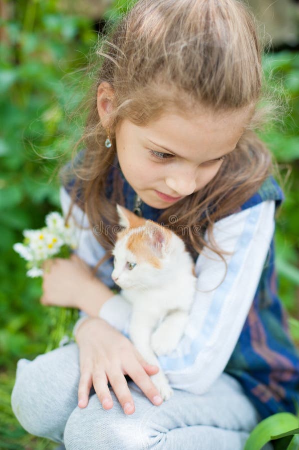 Nettes kleines Mädchen mit einem Blumenstrauß von Gänseblümchenblumen und von kleiner Katze auf ihren Händen lizenzfreie stockfotografie Nettes kleines Mädchen mit einem Blumenstrauß von Gänseblümchenblumen und von kleiner Katze auf ihren Händen lizenzfreie stockfotografie