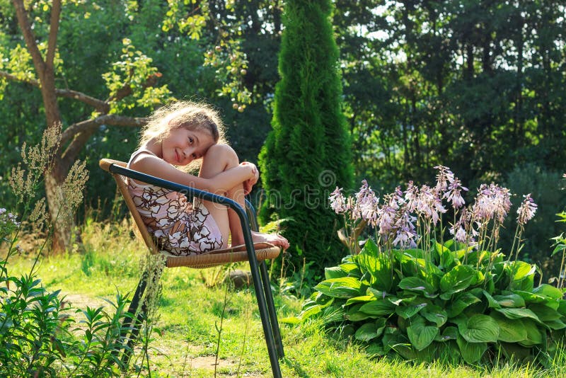 Nettes Kleines Mädchen Sitzt Im Garten Und Lächelt in Warmem Stockfoto