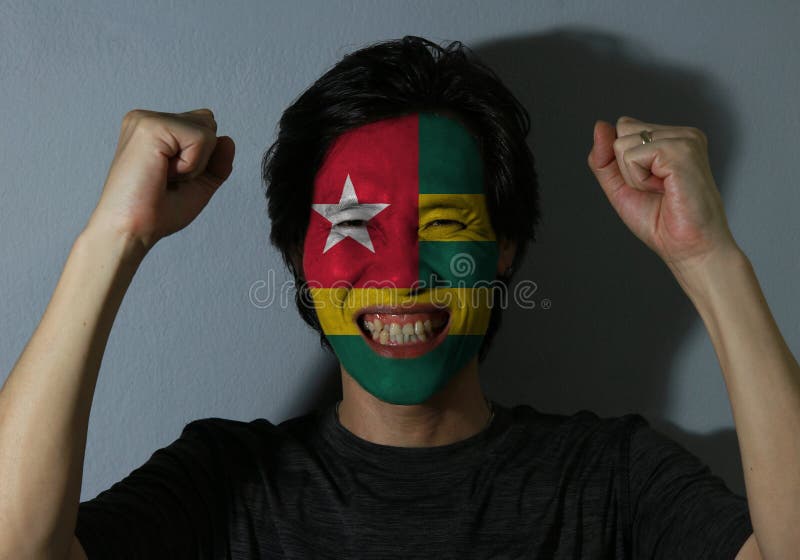 Nettes Porträt eines Mannes mit der Flagge von Togo malte auf seinem Gesicht auf grauem Hintergrund Das Konzept des Sports oder d lizenzfreie stockfotos Nettes Porträt eines Mannes mit der Flagge von Togo malte auf seinem Gesicht auf grauem Hintergrund Das Konzept des Sports oder d lizenzfreie stockfotos
