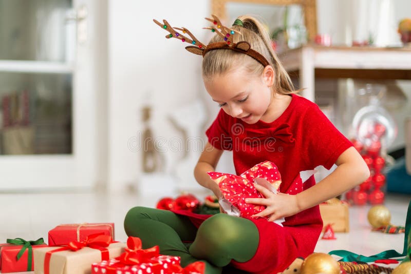 Süßes super aufgeregtes junges Mädchen, das große rote Weihnachtsgeschenke im Wohnzimmer aufmacht. ehrliche Familienfeiertage