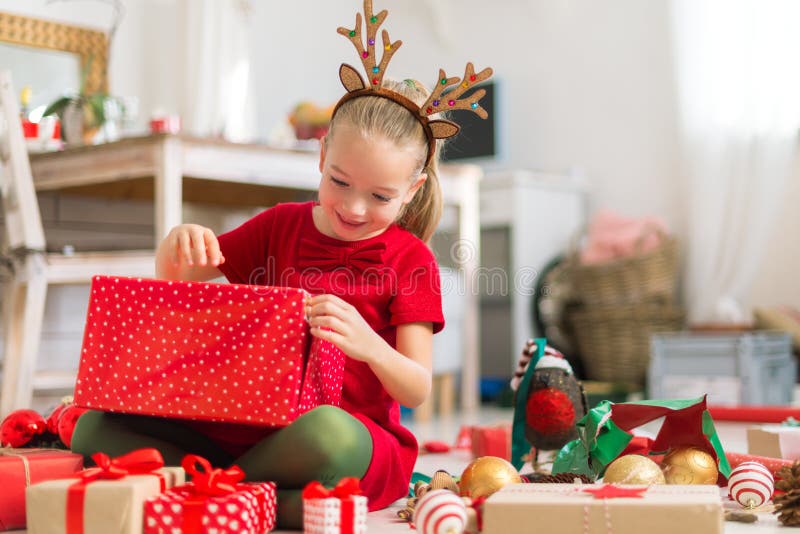 Nettes super aufgeregtes junges Mädchen, das großes rotes Weihnachtsgeschenk beim Sitzen auf Wohnzimmerboden öffnet Offene Famili
