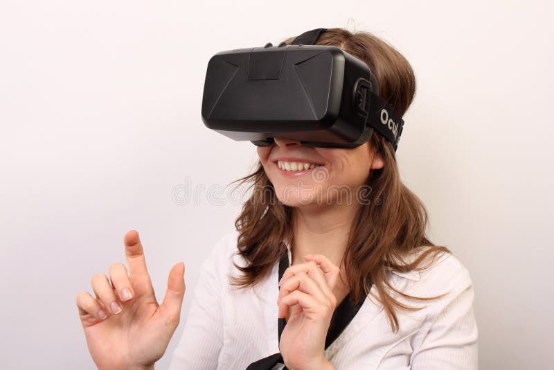 Neugierige, lächelnde Frau in einem weißen Hemd, tragender Kopfhörer virtuellen Realität 3D der Oculus-Riss-VR, etwas erforschend