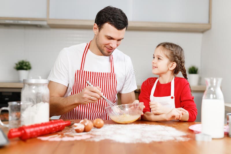 Neugieriges weibliches hübsches Kind hilft ihrem Vater, der Eier mischt, sitzen an der Küche, haben angenehmes Gespräch, genießen stockfotos Neugieriges weibliches hübsches Kind hilft ihrem Vater, der Eier mischt, sitzen an der Küche, haben angenehmes Gespräch, genießen stockfotos