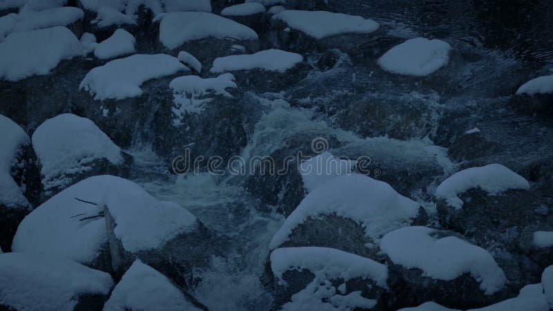 A neve cai sobre o rio rochoso Ã  noite