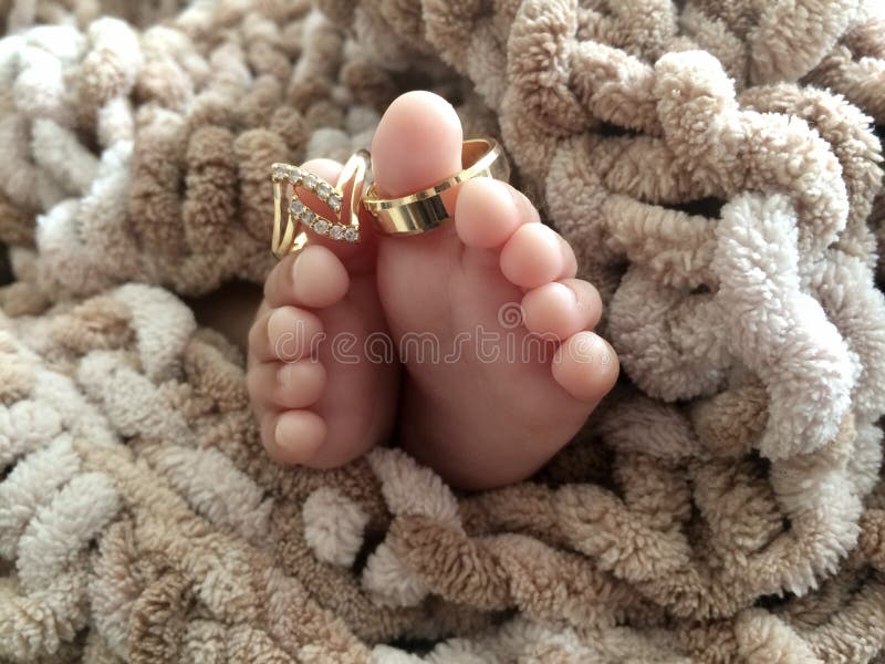 New Born Baby Feet on Brown Blanket with wedding rings. New Born Baby Feet on Brown Blanket with wedding rings.