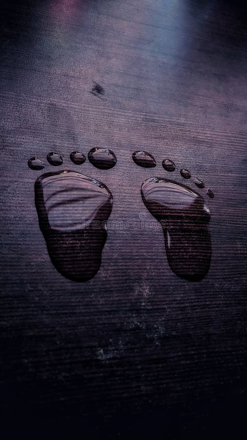 New born baby& x27;s foot print made from water droplets on brown coloured wooden board