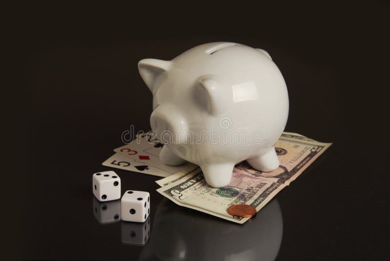 A piggy bank, dice, playing cards and money on black representing the gamble of the new economy. A piggy bank, dice, playing cards and money on black representing the gamble of the new economy